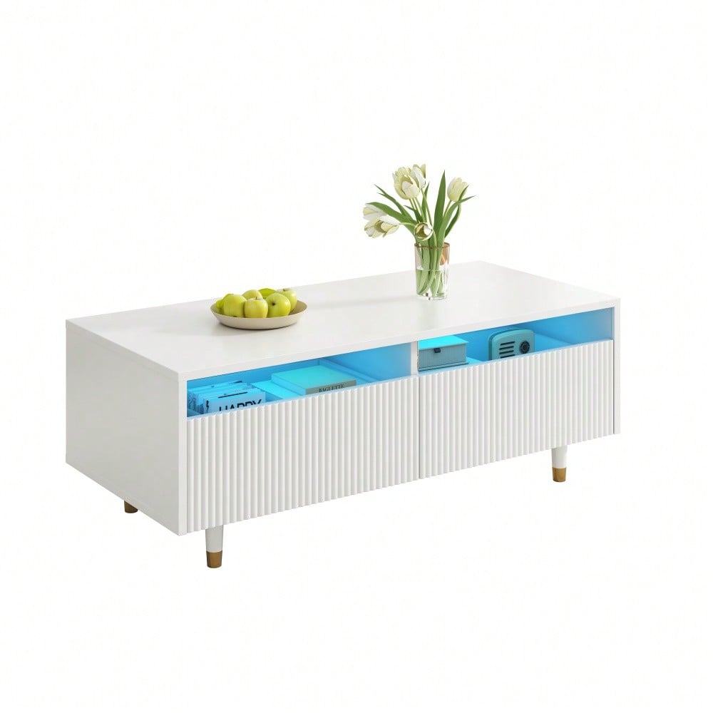 Dieser moderne LED-Couchtisch verfügt über eine gewellte Schubladenplatte, gold-weiße Beine, zwei Schubladen und einen farbwechselnden LED-Lichtstreifen. Ein passender TV-Schrank ist ebenfalls erhältl