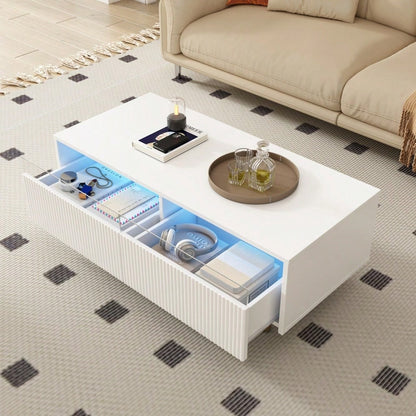 Dieser moderne LED-Couchtisch verfügt über eine gewellte Schubladenplatte, gold-weiße Beine, zwei Schubladen und einen farbwechselnden LED-Lichtstreifen. Ein passender TV-Schrank ist ebenfalls erhältl