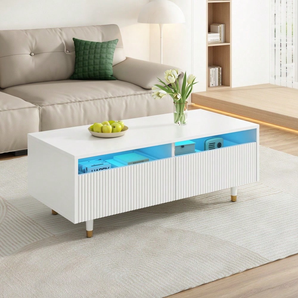 Dieser moderne LED-Couchtisch verfügt über eine gewellte Schubladenplatte, gold-weiße Beine, zwei Schubladen und einen farbwechselnden LED-Lichtstreifen. Ein passender TV-Schrank ist ebenfalls erhältl